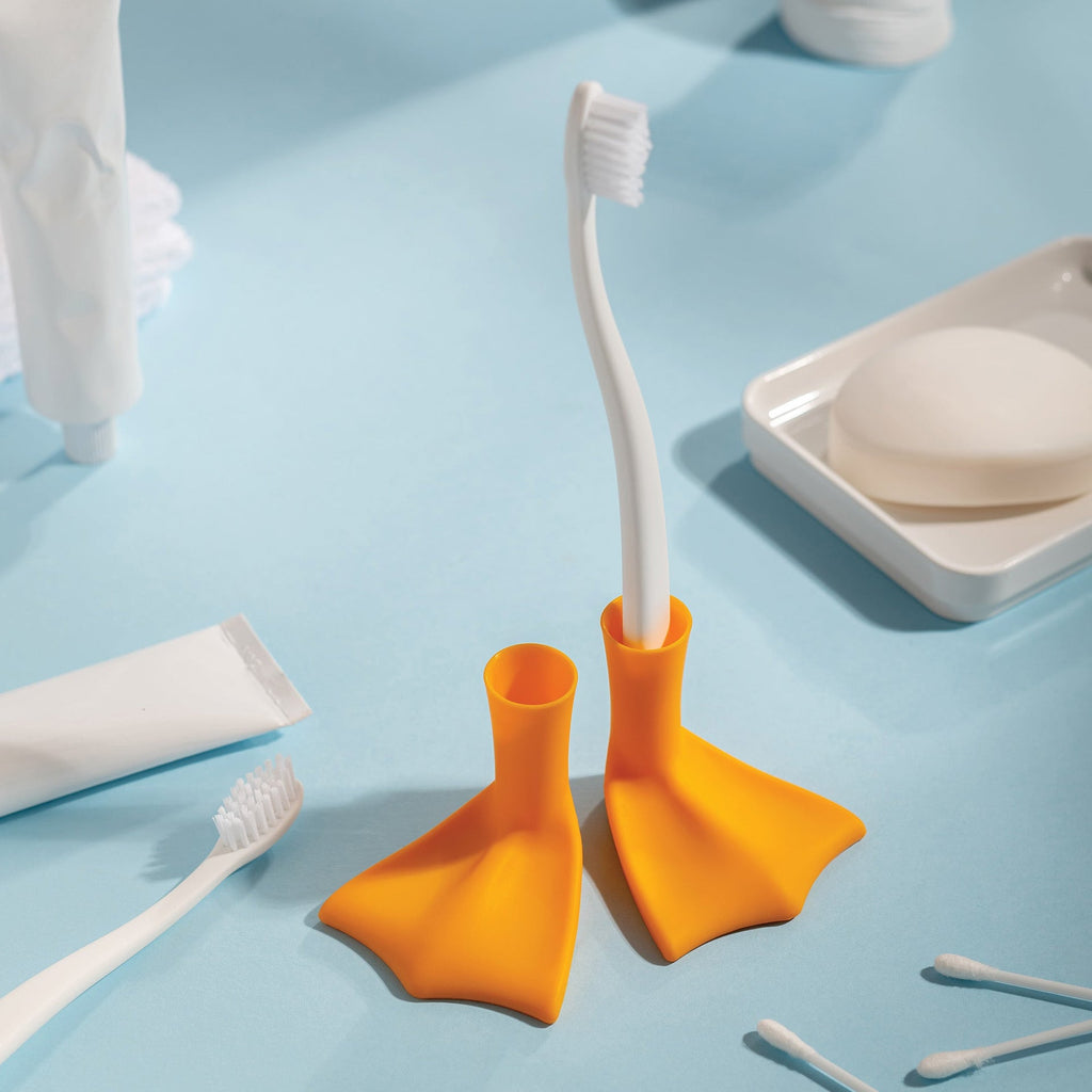 Two Duck-Clean toothbrush holders with orange feet are on a blue bathroom surface.